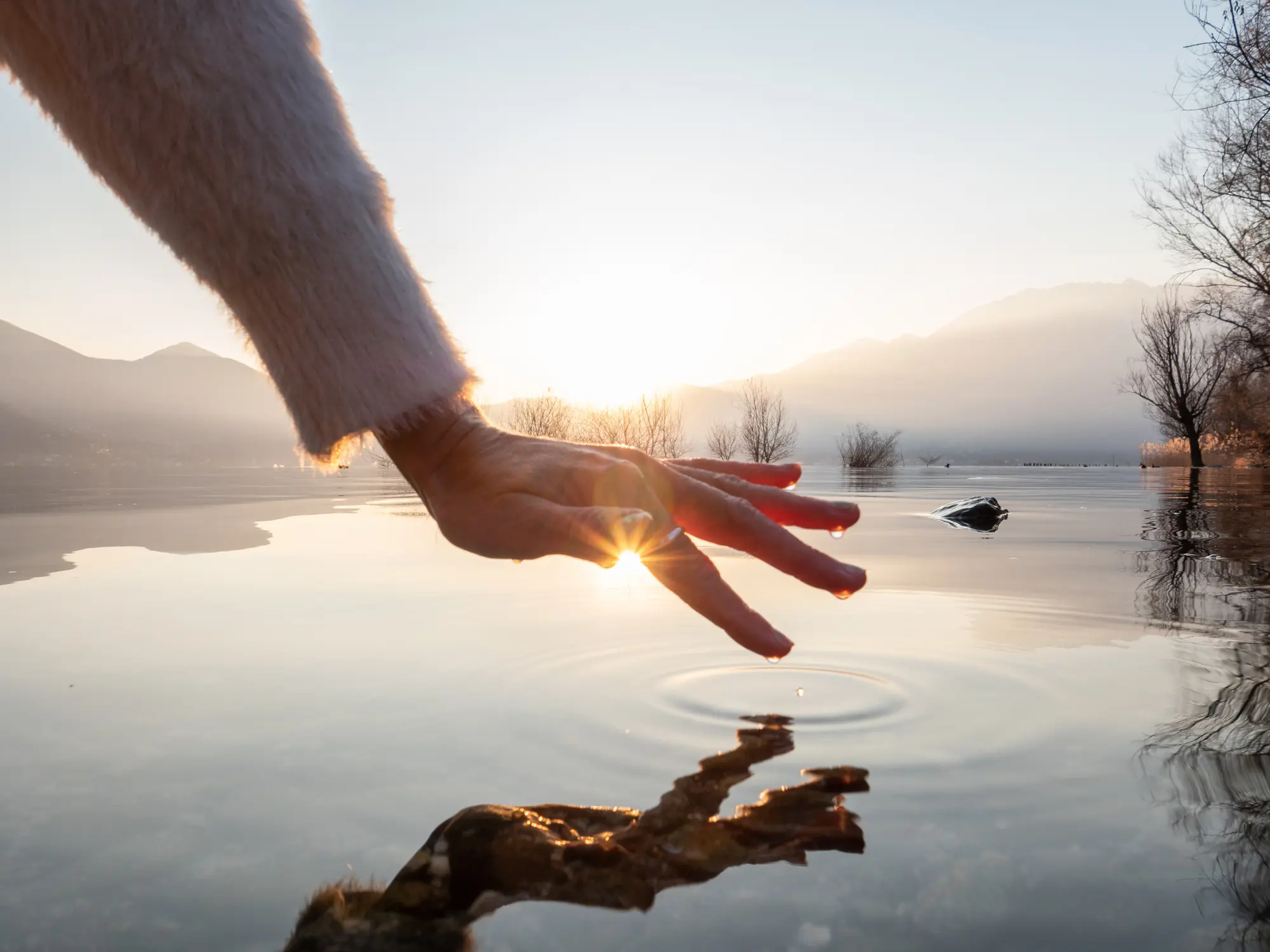 Hand skimming lake surface at sunrise